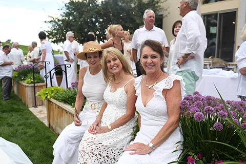 Three ladies in white dresses at an outdoor event.